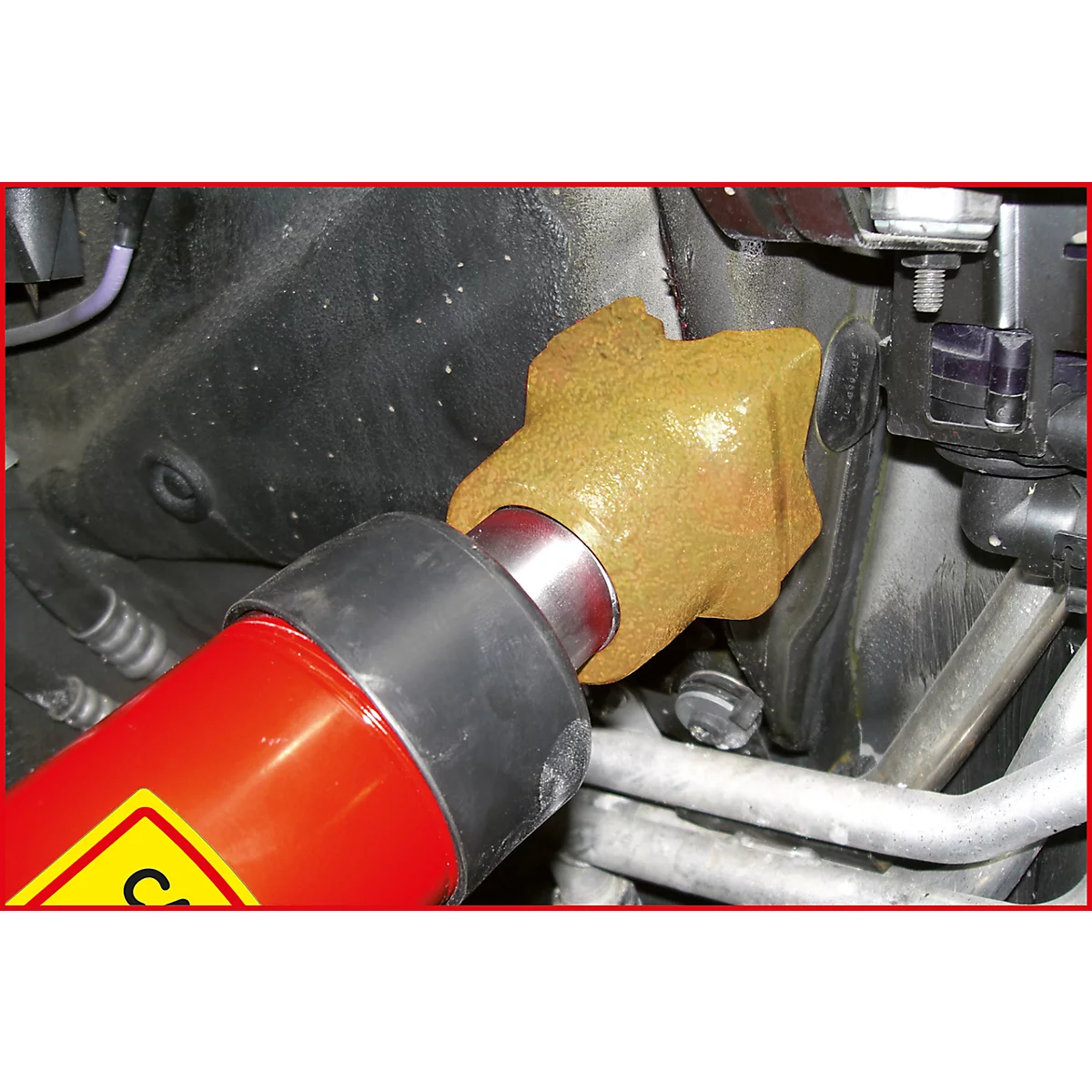 Nahaufnahme einer rot-gelben Spezialwerkzeugs, das an einem Motor befestigt ist. Die Werkzeugspitze ist goldfarben.